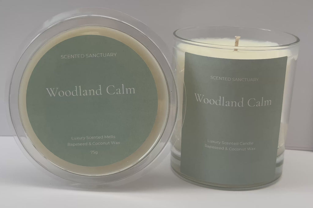 Product showcase video of the Woodland Calm range: a clear 75g wax melt clamshell and a 220g clear glass candle, both featuring minimalist sage green labels with white text. Audio voiceover details the fresh herbal, cedarwood, amber, moss, and patchouli fragrance notes.