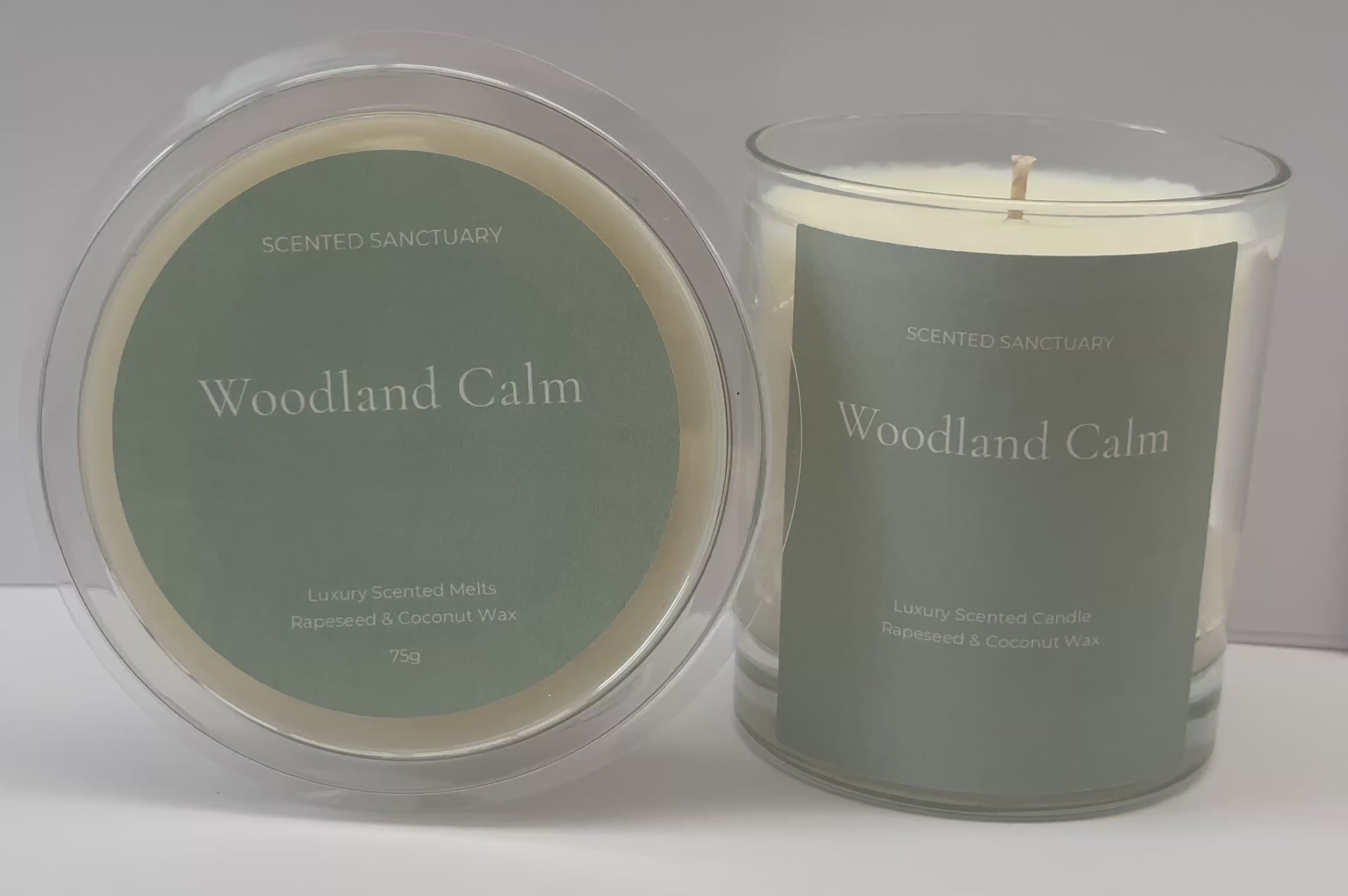Product showcase video of the Woodland Calm range: a clear 75g wax melt clamshell and a 220g clear glass candle, both featuring minimalist sage green labels with white text. Audio voiceover details the fresh herbal, cedarwood, amber, moss, and patchouli fragrance notes.